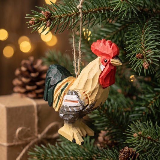 A handcrafted wooden rooster Christmas ornament hanging from a pine tree branch, with warm bokeh lights and a wrapped gift in the background.