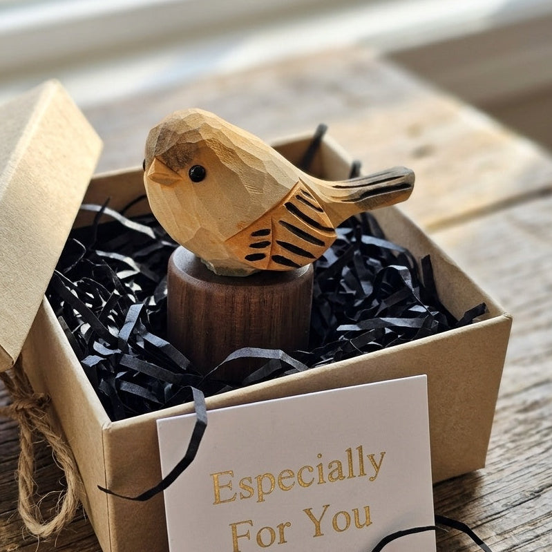 A small carved wooden bird figurine displayed inside an open kraft gift box with black shredded paper filler and a card that reads 'Especially For You'.