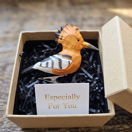 Side view of a hand-carved, hand-painted wooden Hoopoe clip-on bird ornament perched in black shredded paper inside an open kraft gift box, alongside a card reading 'Especially For You'.