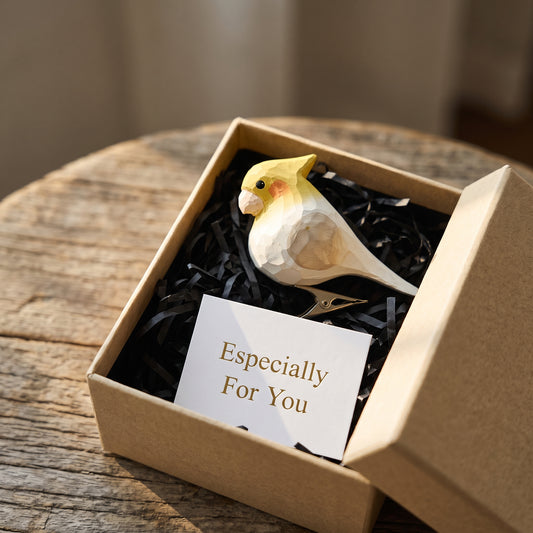 Hand-carved white wooden cockatiel ornament nestled in an open kraft gift box filled with black crinkle paper, beside an "Especially For You" card on a rustic wood surface.