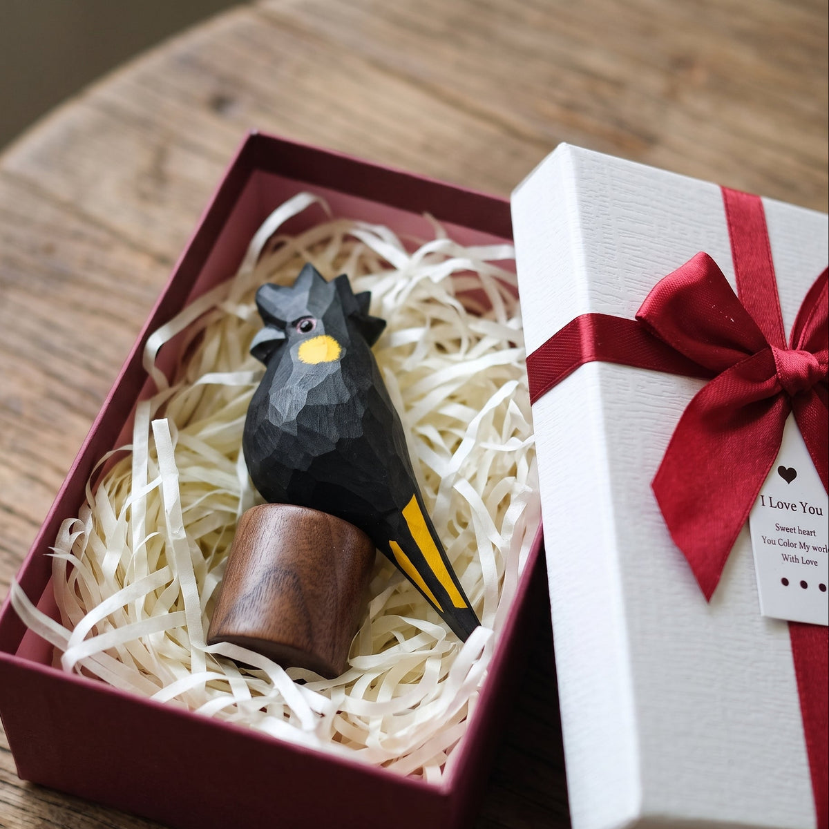 Hand-carved basswood Yellow-tailed Black Cockatoo figurine packaged inside a red gift box with ribbon and gift tag