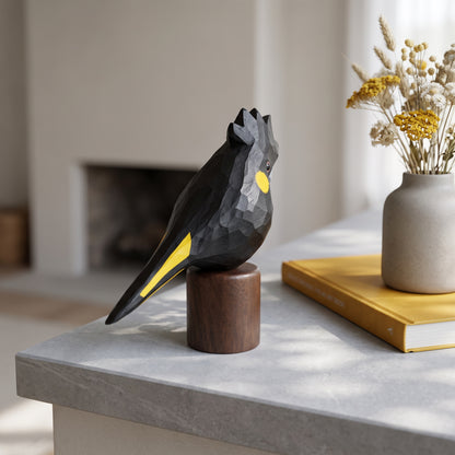 Handcrafted basswood Yellow-tailed Black Cockatoo statuette on round black walnut base in a modern home decor setting