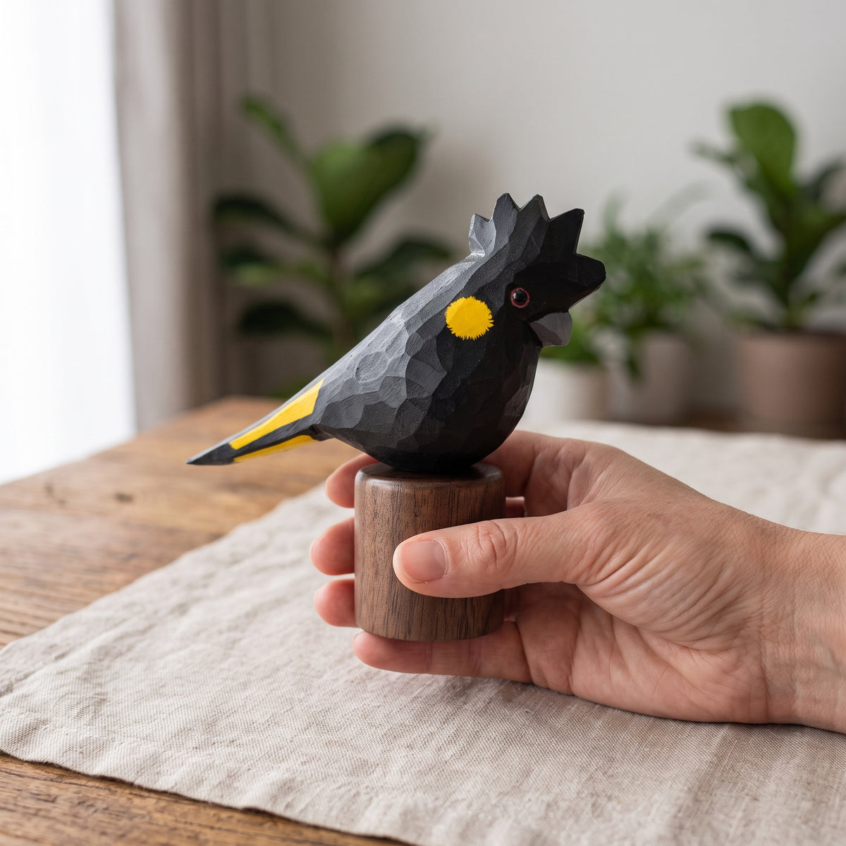 Hand holding hand-carved basswood Yellow-tailed Black Cockatoo statuette on round black walnut stand
