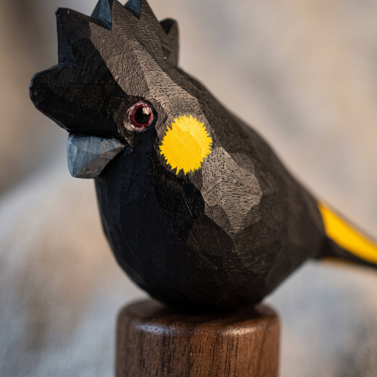 Macro close-up of hand-painted basswood Yellow-tailed Black Cockatoo bird head and cheek details on walnut base