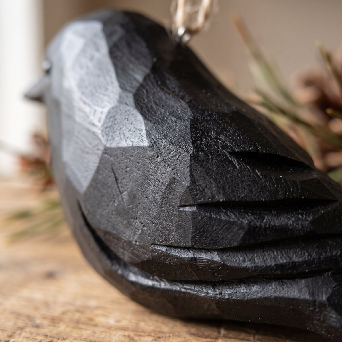 A close-up of a faceted bird-shaped Crow ornament in dark charcoal gray and black, resting on a rustic wooden surface with a soft blurred background.