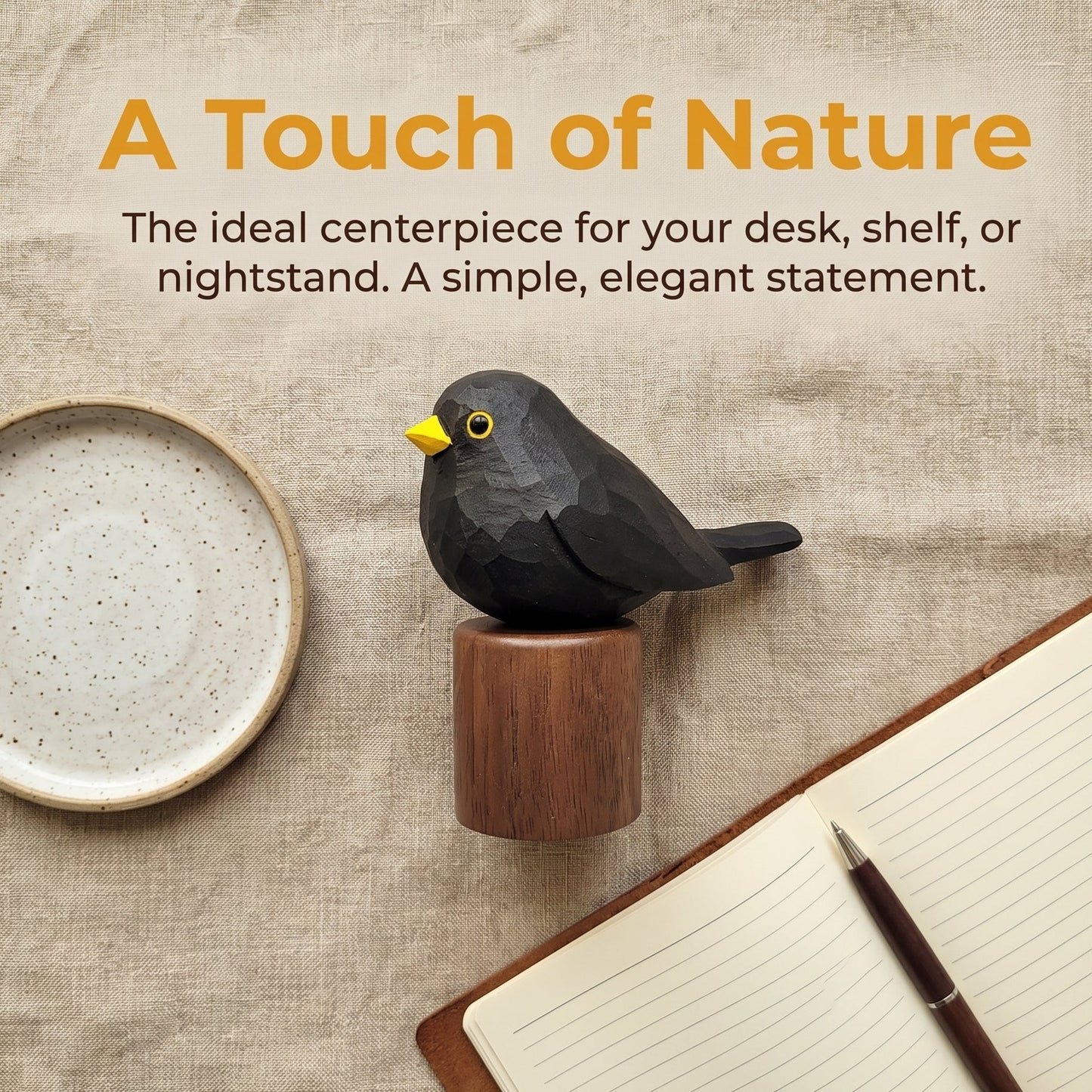 A Eurasian Blackbird-shaped desk accessory with a yellow beak and small wooden base, styled on a linen surface with a ceramic dish, open notebook, and pen. Text at the top reads 'A Touch of Nature' with descriptive copy.