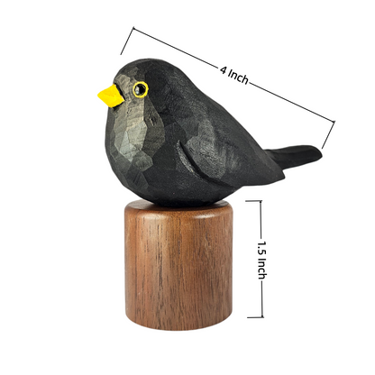 A carved Eurasian Blackbird figurine with a yellow beak and eye, mounted on a brown wooden cylinder base, shown on a white background with dimension lines indicating 4 inch length and 1.5 inch height.