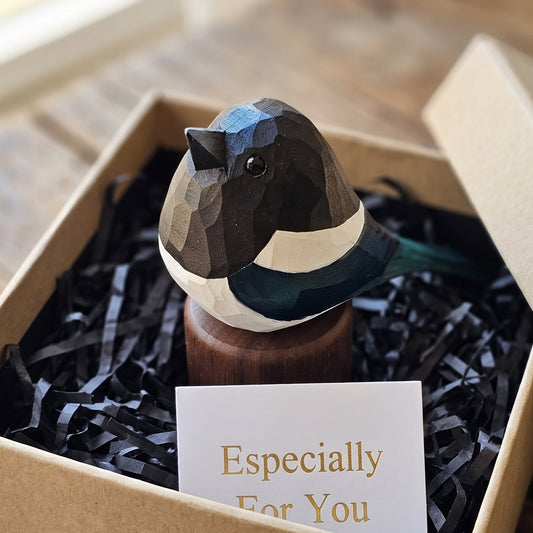 A geometric Eurasian magpie figurine displayed in a kraft gift box with black shredded paper filler and a small card that reads 'Especially For You'. The bird has faceted dark gray, black, white, and teal-blue sections.