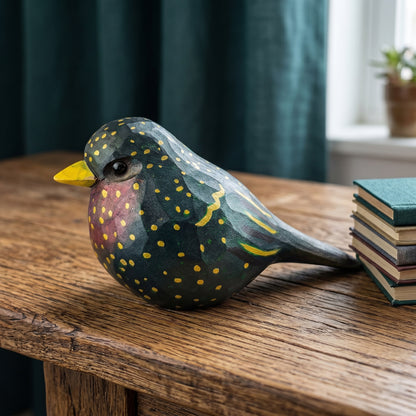 Hand-carved wooden European Starling figurine resting on a rustic wooden table next to a stack of vintage books by a window