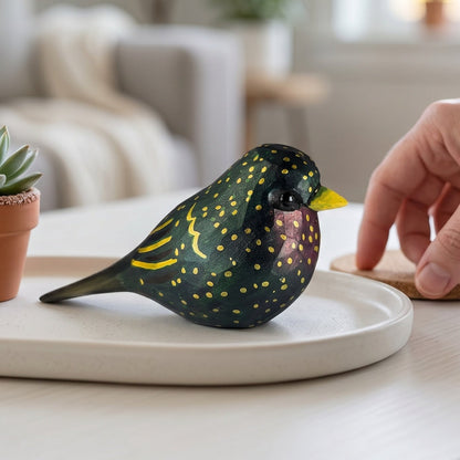 Hand-carved wooden European Starling figurine on a white ceramic tray next to a small potted succulent