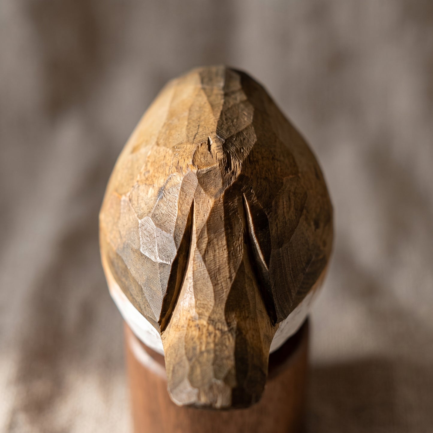 A close-up of a hand-carved wooden European robin figurine, likely a woodpecker, with detailed natural wood grain and a white band at the base, set against a blurred gray background.