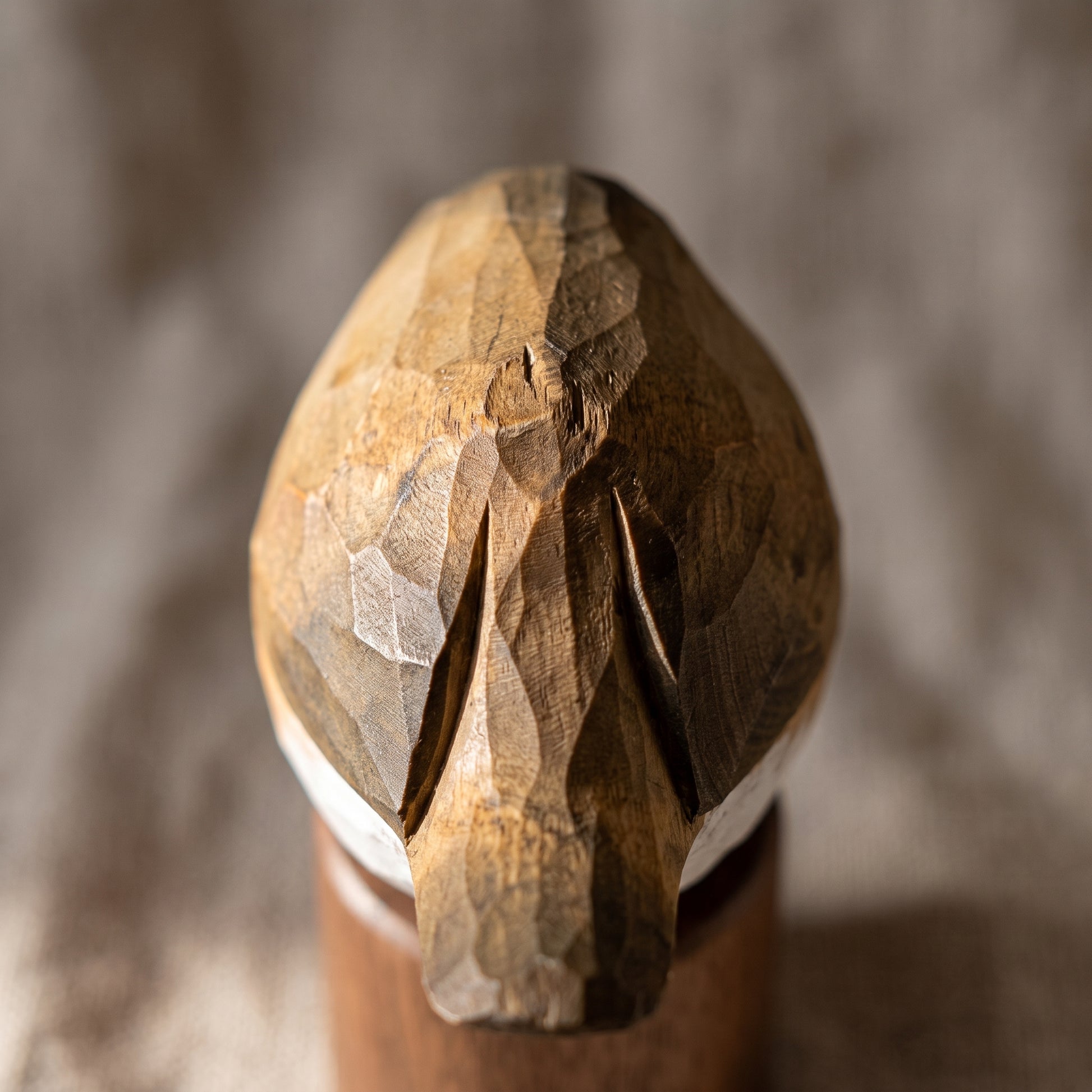 A close-up of a hand-carved wooden European robin figurine, likely a woodpecker, with detailed natural wood grain and a white band at the base, set against a blurred gray background.