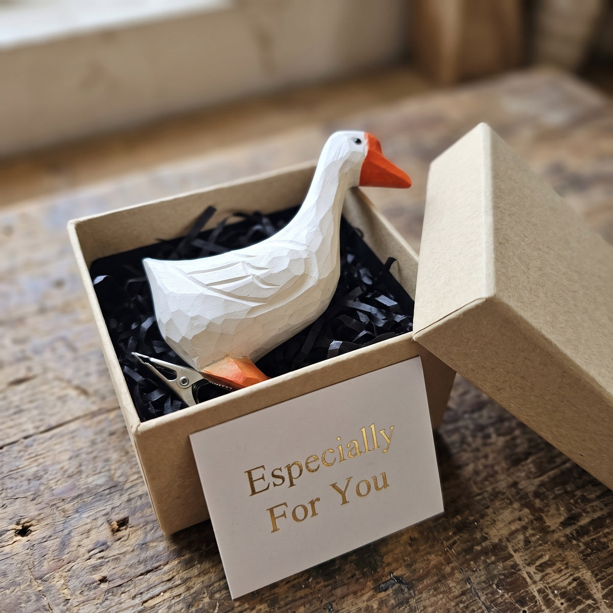A white geometric paper-cut style goose figurine with an orange beak sits inside a kraft gift box filled with black shredded paper. A small card reading 'Especially For You' is placed in front of the box, and the box lid leans open to the right.