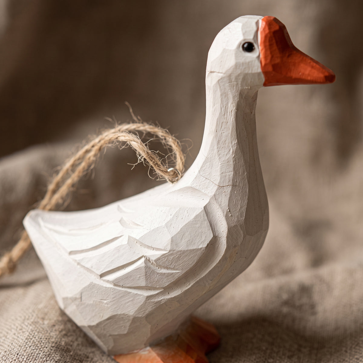 Hand-carved white goose wooden ornament with jute loop resting on a textured fabric surface