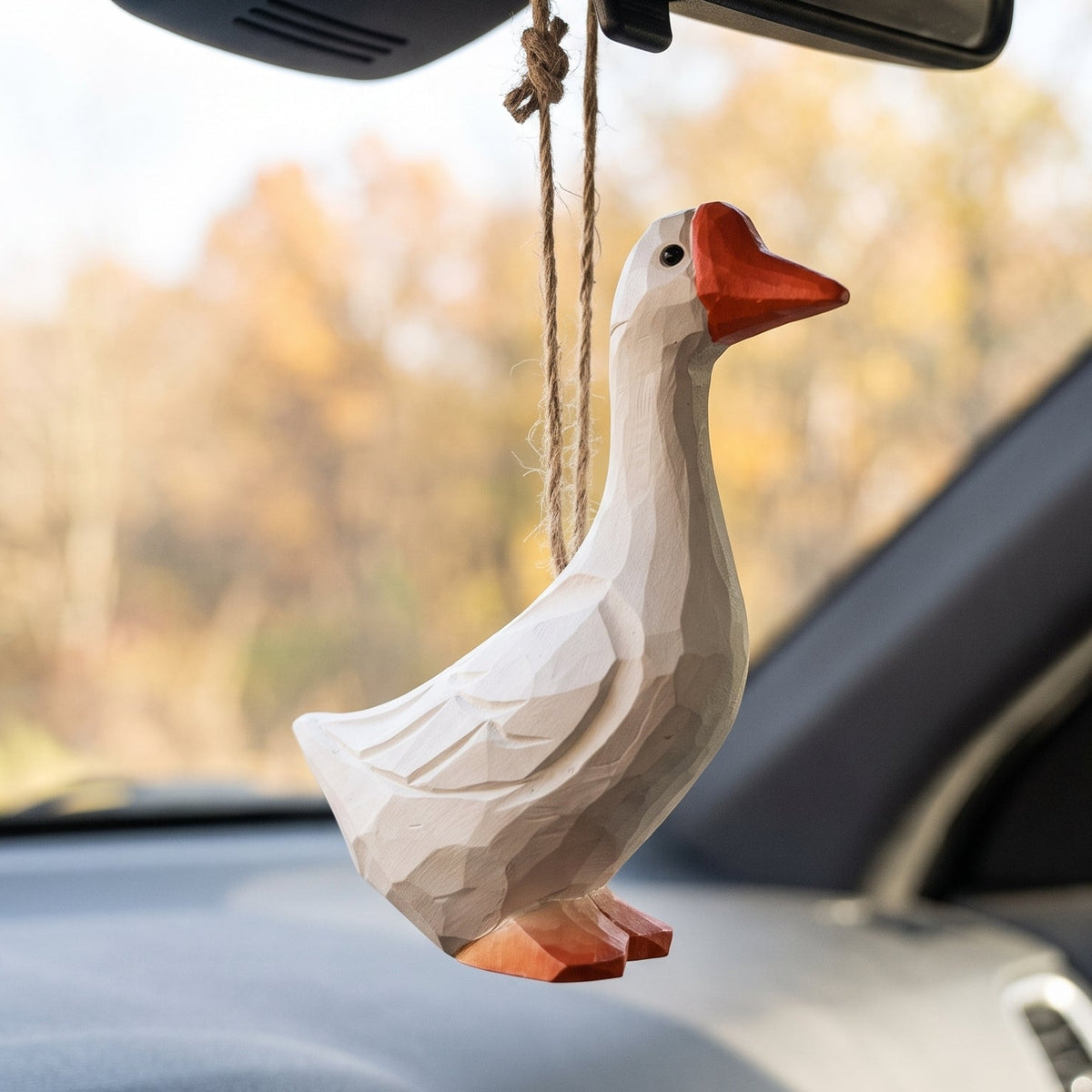 Hand-carved white goose wooden ornament hanging from a car rearview mirror