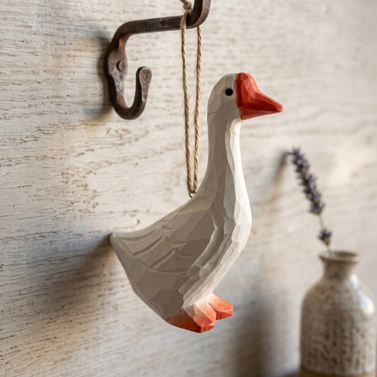 Hand-carved white goose wooden ornament hanging from a rustic metal hook