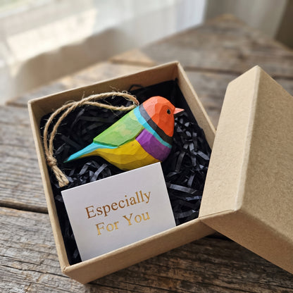 A colorful wooden Gouldian finch ornament with a string loop, presented in a kraft gift box with black shredded paper and a card that reads 'Especially For You'.