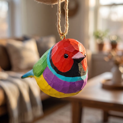 A colorful Gouldian finch-shaped hanging ornament with a geometric, faceted texture, suspended by a natural jute string in a cozy, softly blurred living room setting.