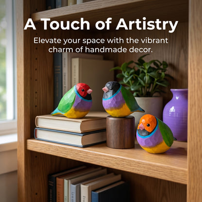 Three colorful wooden Gouldian finch figurines displayed on a wooden bookshelf alongside books, a small potted plant, and a purple vase, with the text 'A Touch of Artistry' at the top.