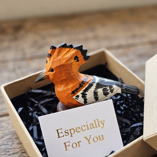 A small carved Hoopoes figurine with an orange crest and black-and-white patterned body sits in a kraft gift box filled with black shredded paper and a card that reads 'Especially For You,' placed on a wooden surface.