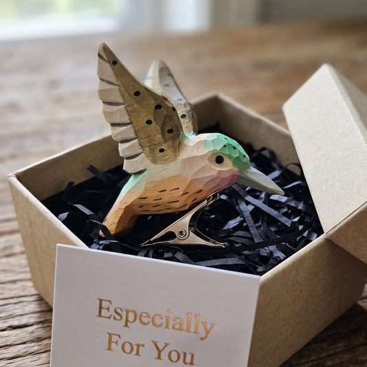 Hand-carved wooden clip-on hummingbird ornament with green head, tan body, and metal clip displayed inside an open kraft gift box with a card reading "Especially For You".