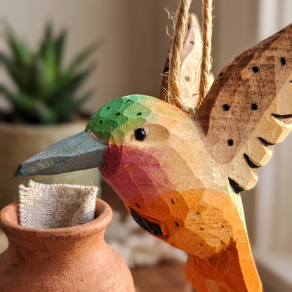 Close-up of a hand-carved wooden hummingbird ornament hanging above a small terracotta pot.