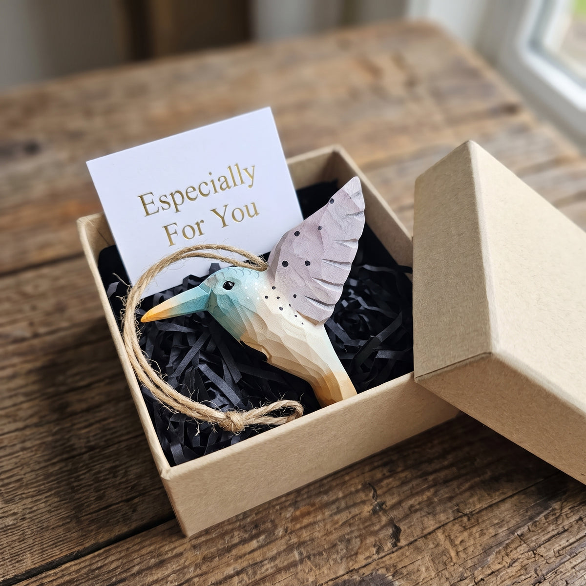 Hand-carved wooden hummingbird ornament packaged in a kraft gift box with black paper shred and an "Especially For You" card.