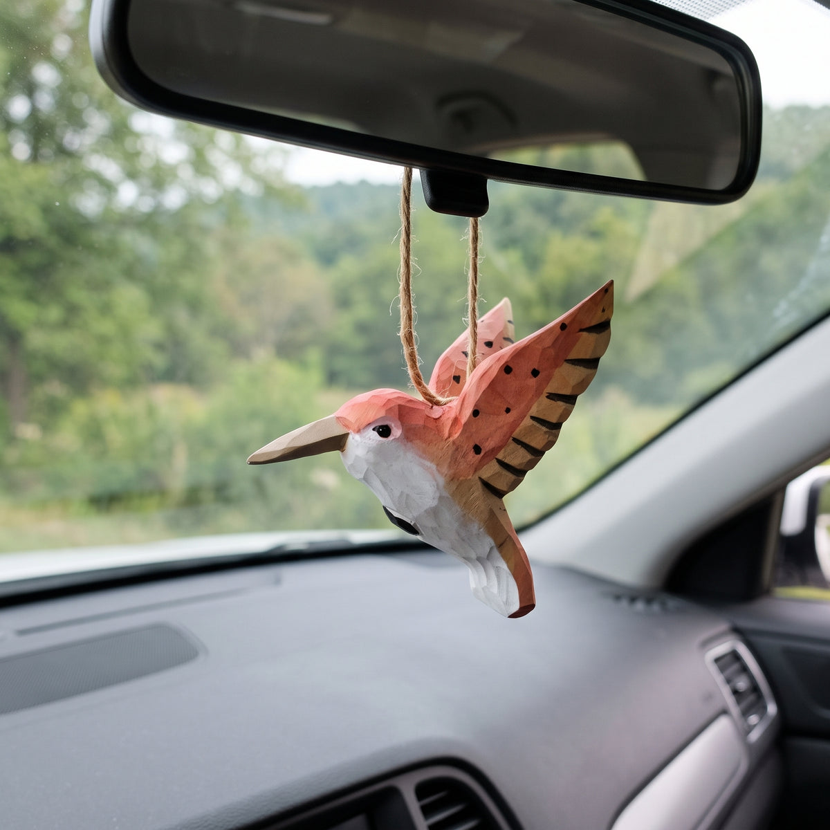 Hand-carved wooden hummingbird ornament hanging from a car rearview mirror.