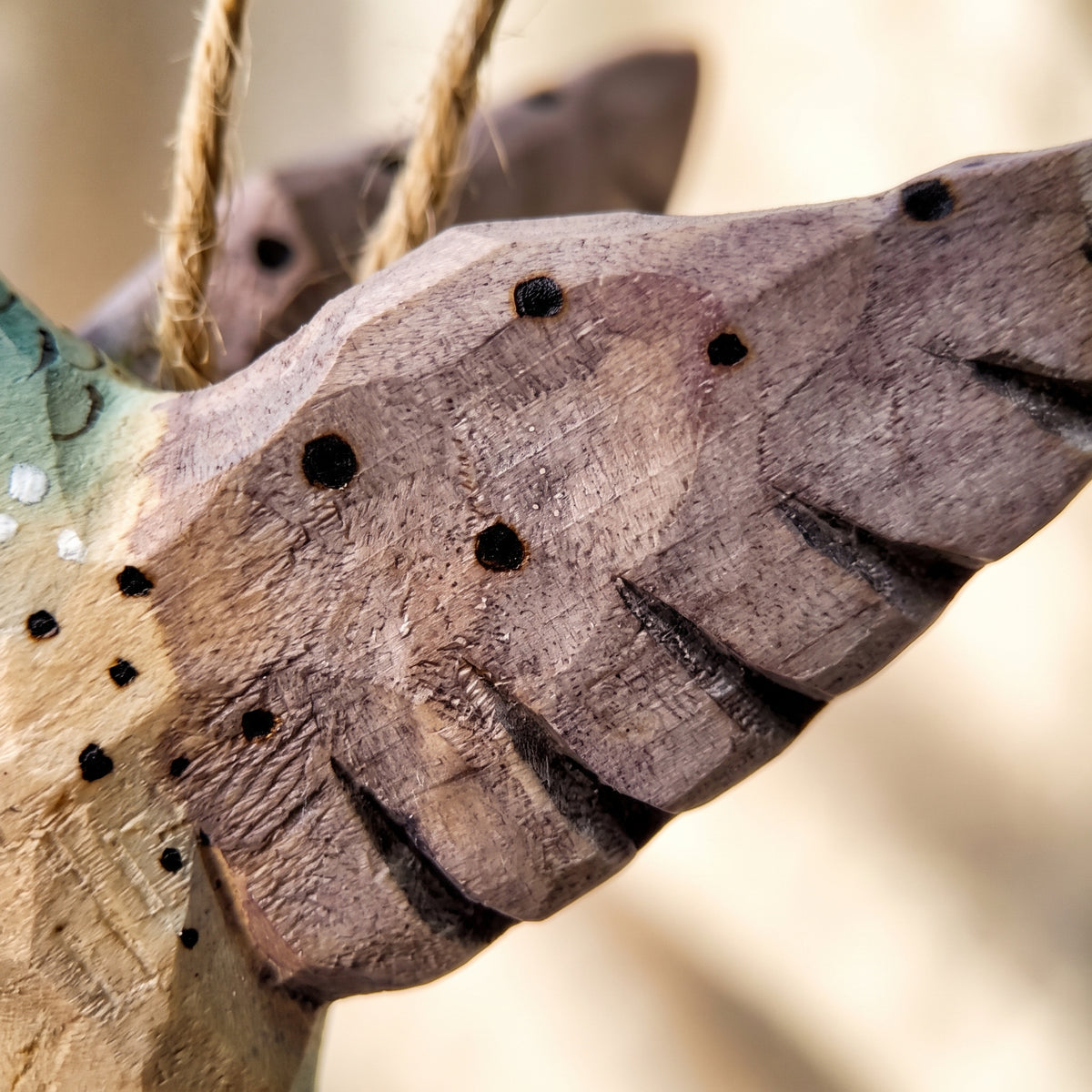 Extreme close-up of a hand-carved wooden hummingbird ornament showing wood grain and carved wing details.