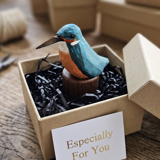 A small painted Kingfisher figurine in a kraft gift box with black paper shred, a card reading 'Especially For You,' and a rustic wooden table in the background.