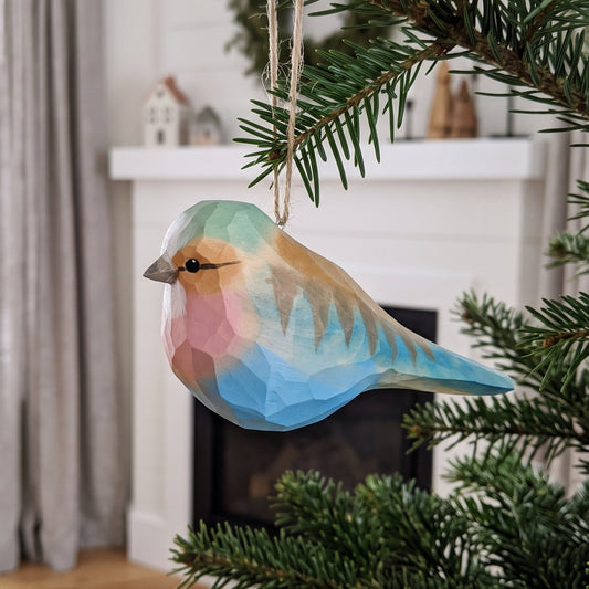 Hand-carved basswood Lilac-Breasted Roller ornament with soft blue and pink plumage hanging from a pine branch