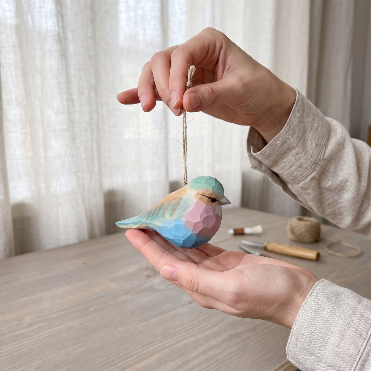 Hands holding a hand-carved basswood Lilac-Breasted Roller ornament suspended by its twine loop