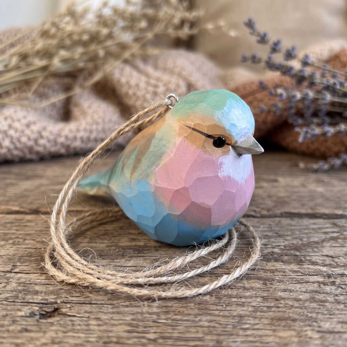 Hand-carved basswood Lilac-Breasted Roller ornament resting on a rustic wooden table with coiled twine