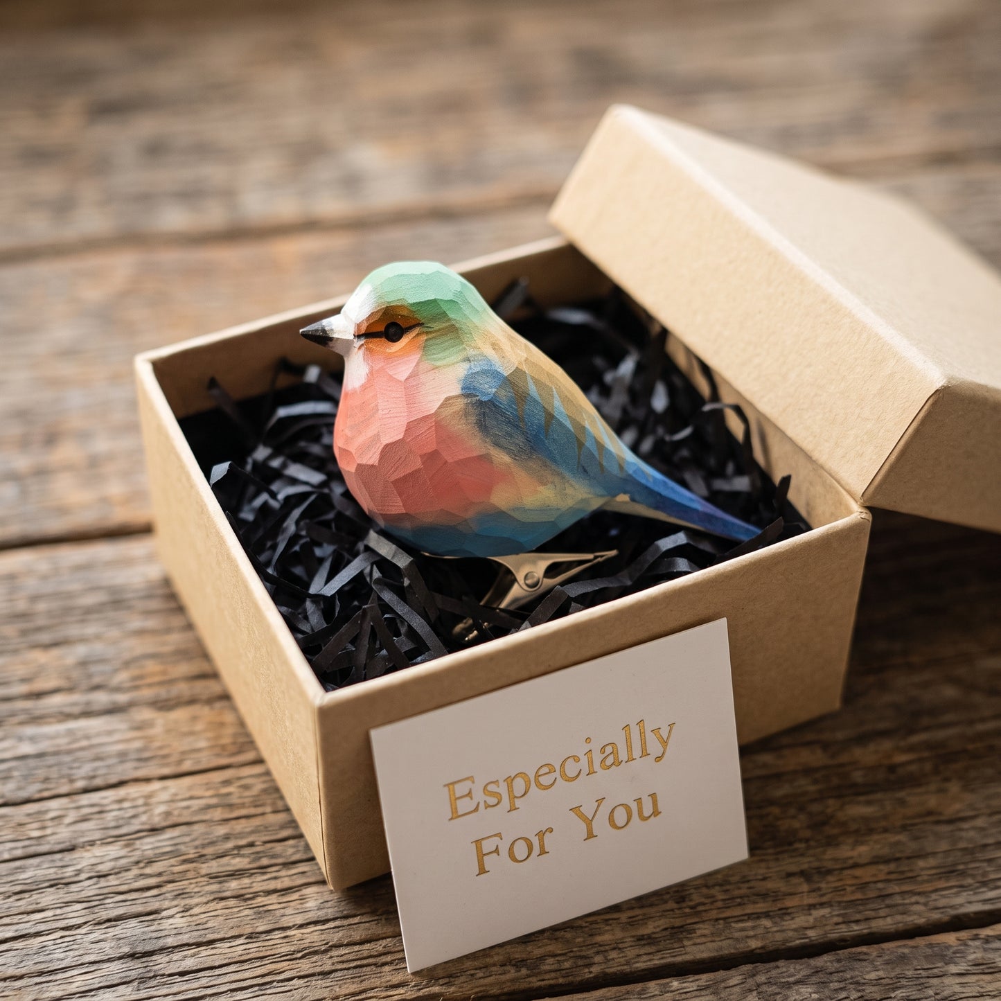 Hand-carved, hand-painted wooden Lilac-Breasted Roller clip-on bird ornament with colorful plumage, displayed inside an open kraft gift box filled with black shredded paper alongside a card reading 'Especially For You'.