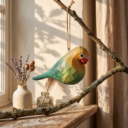 A colorful geometric Lovebirds ornament hangs from a rustic tree branch on a wooden windowsill, styled with a small vase of dried lavender and a glass bottle in warm natural light.