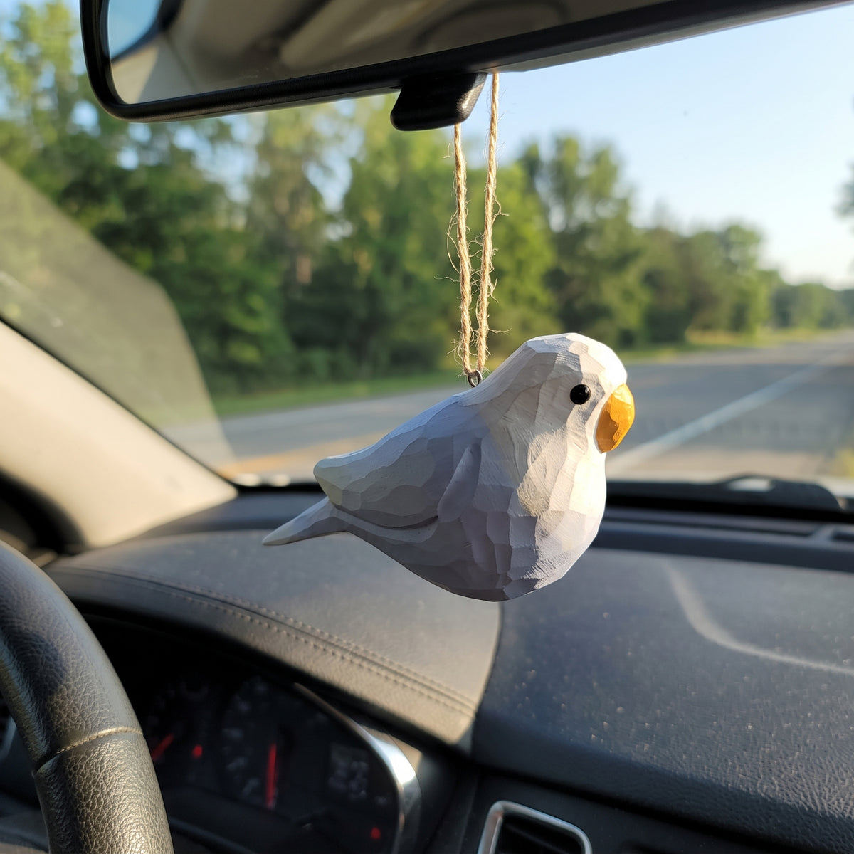 A small white Lovebirds-shaped car air freshener with a yellow beak hangs from a string in a car dashboard.