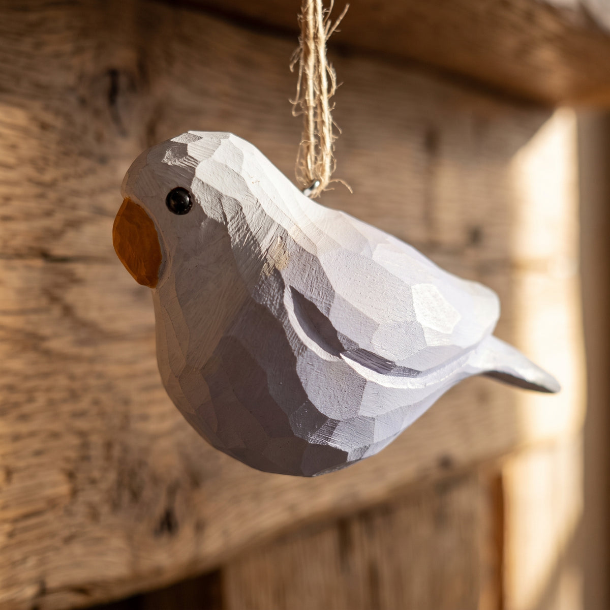 A handcrafted wooden Lovebirds ornament with a geometric, faceted design, hanging from a jute twine string against a rustic wooden background.