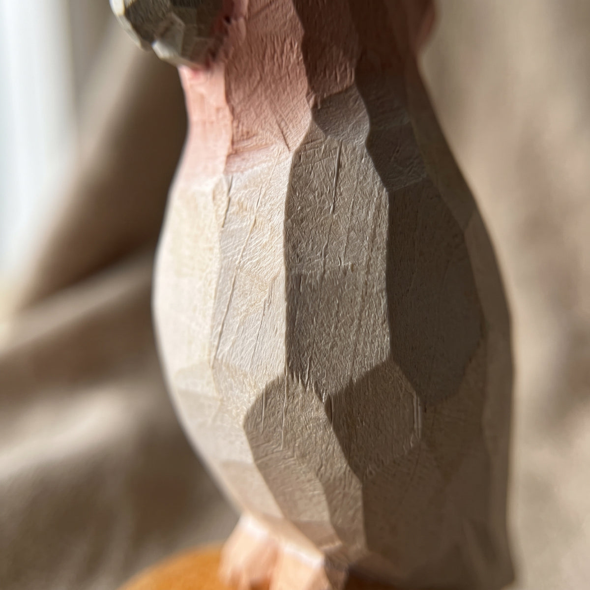Close-up of the hand-carved wood body details on a Pink Cockatoo bird figurine, showcasing faceted knife cuts and natural grain texture.