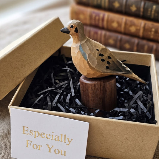 A carved wooden Mourning Dove figurine displayed inside a kraft gift box with black shredded paper filler and a card that reads 'Especially For You.' The bird has a light natural wood body with dark eye and beak details, spotted wing patterns, and a small blue accent on its back, mounted on a dark wooden base.