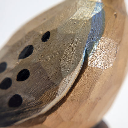 Close-up of a handcrafted wooden Mourning Dove with a metallic gold leaf finish, featuring a series of black circular cutouts on the left side.