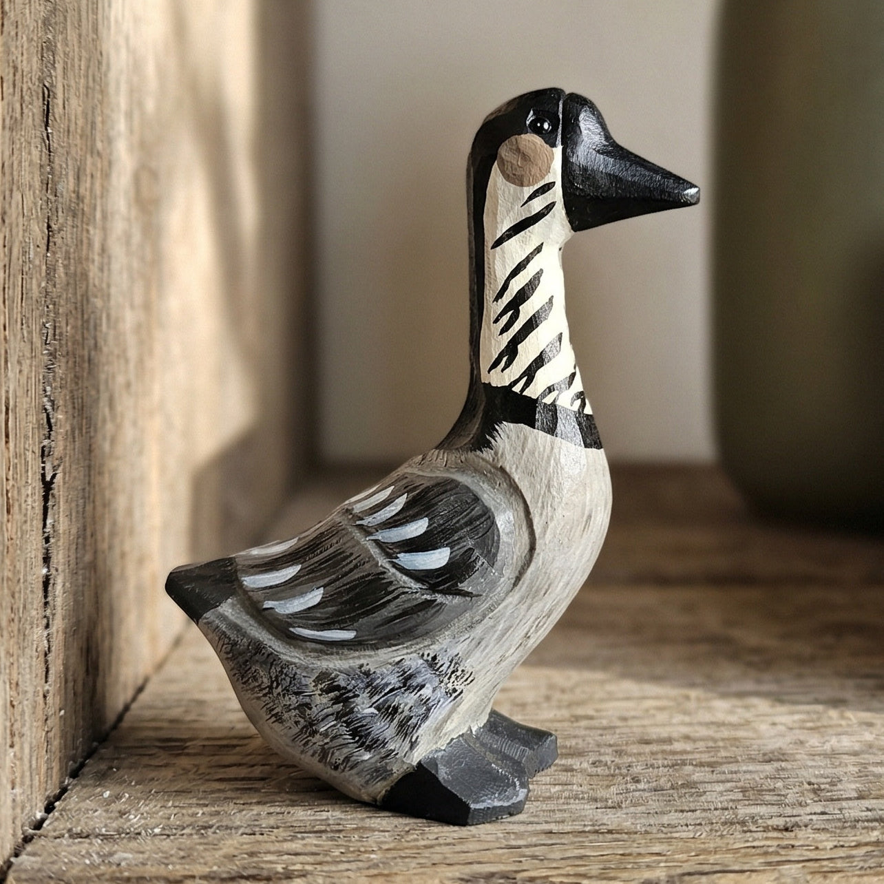 A small hand-carved wooden Hawaiian Goose figurine with black, white, and gray painted details, standing on a rustic wooden surface.