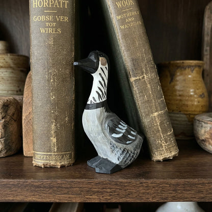 A small carved wooden Hawaiian Goose figurine with black and white feather details, displayed on a dark wooden shelf between vintage books.