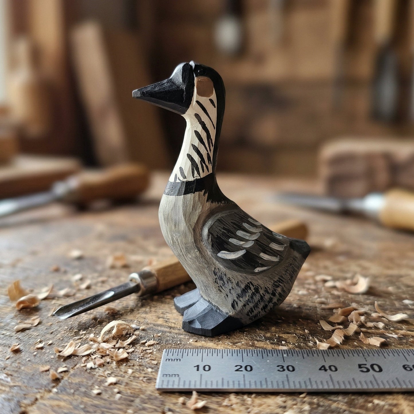 A hand-carved wooden Hawaiian Goose figurine with black, white, and gray painted details, displayed on a wooden workbench with carving tools and wood shavings in the background.