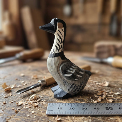 A hand-carved wooden Hawaiian Goose figurine with black, white, and gray painted details, displayed on a wooden workbench with carving tools and wood shavings in the background.