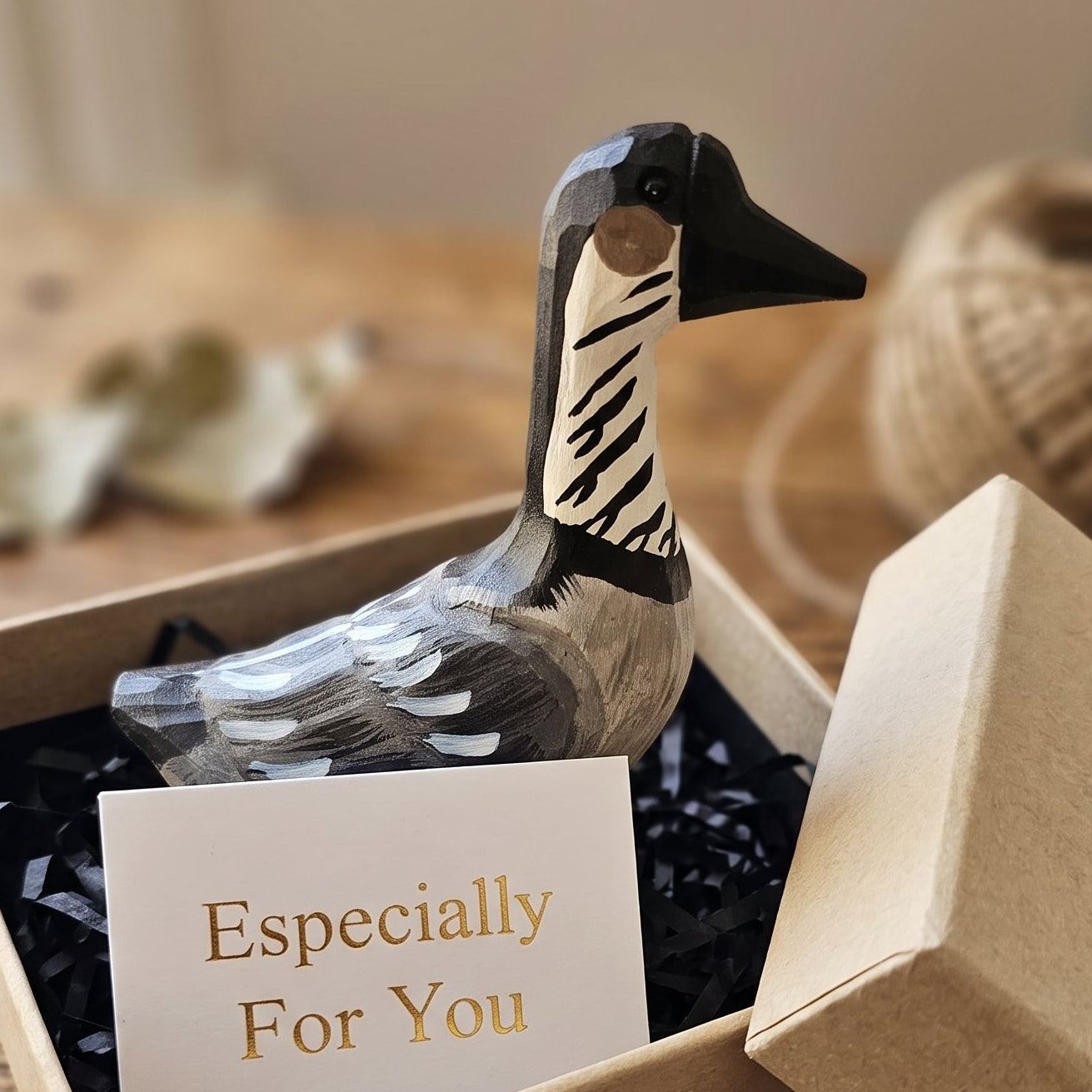 A handcrafted wooden Hawaiian Goose figurine with a black and white striped neck, presented in a kraft gift box with black crinkle paper and an 'Especially For You' card, set on a rustic wooden table.