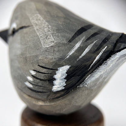 Close-up of a carved wooden Northern mockingbird sculpture with black and white painted details, mounted on a small round wooden base against a light gray background.