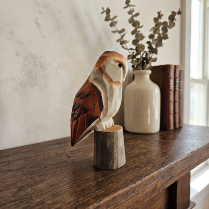 Hand-carved wooden barn owl statue on a rustic wooden sideboard next to a ceramic vase and antique books