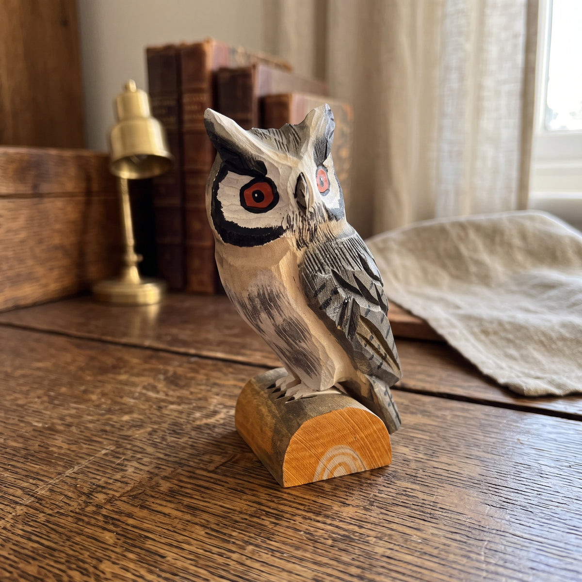 Handcrafted basswood Northern white-faced owl figurine on a natural wood log base displayed on a rustic wooden desk