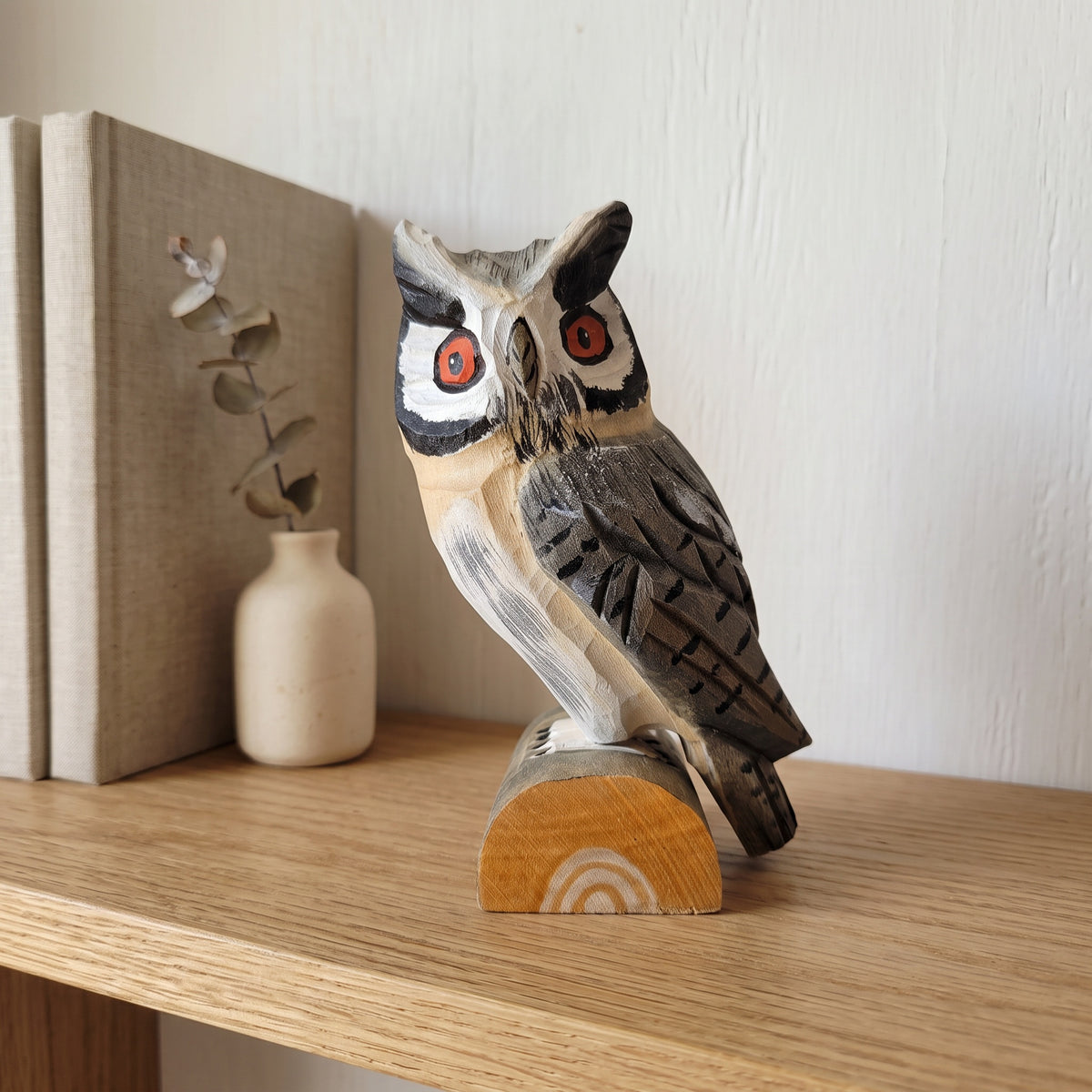 Handmade wooden owl figurine displayed on a shelf next to books and houseplants