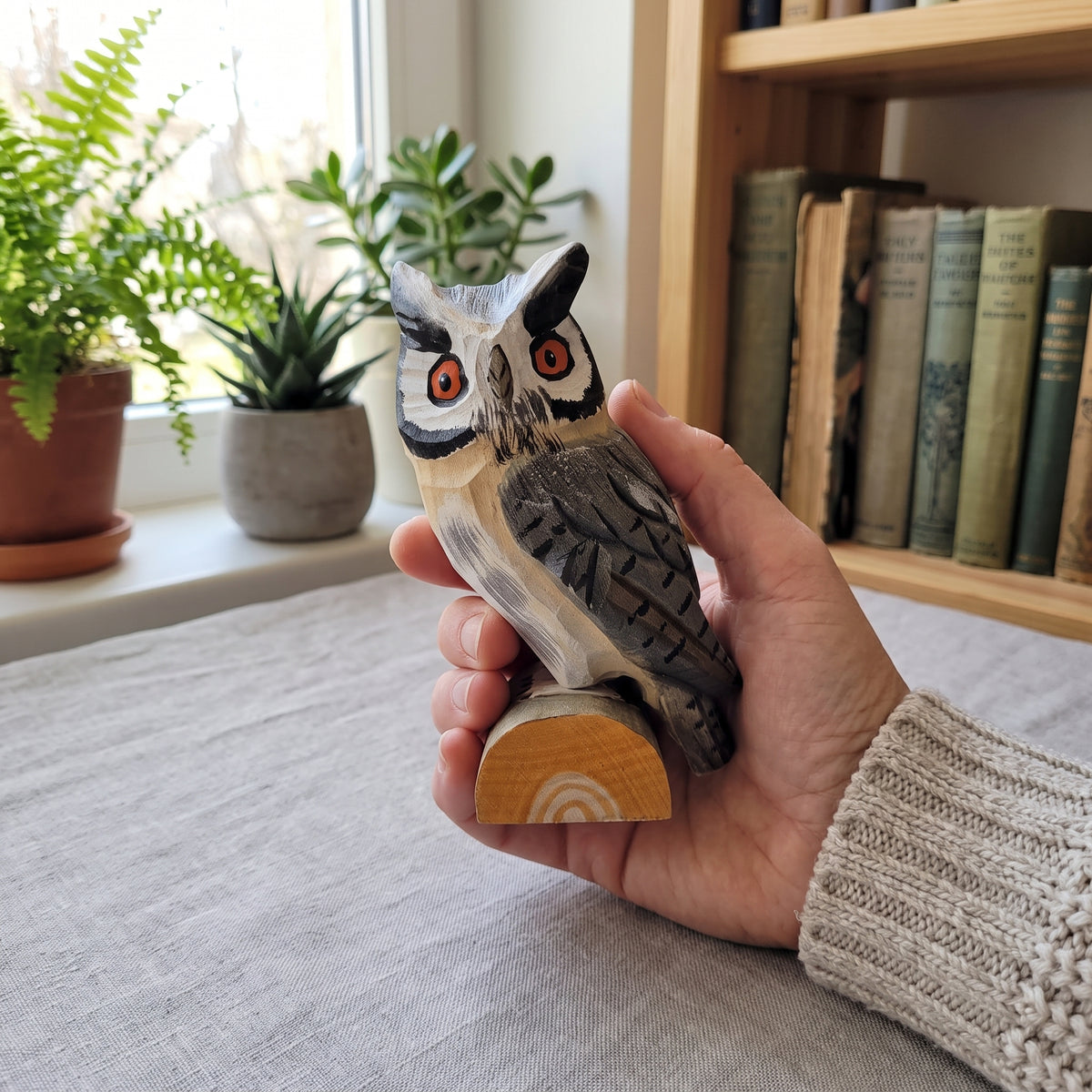 Hand holding a handcrafted 4.5 inch basswood Northern white-faced owl figurine on a natural wood log base